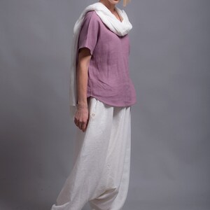 May include: A woman wearing a mauve linen top with a white linen scarf and white linen pants. The pants have a loose, wide-leg style. The text "shantimama URBAN FOLK WEAR" is visible at the top of the image.