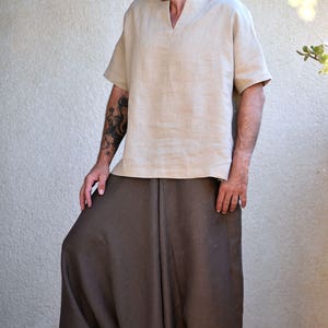 A person wearing a light brown linen shirt with a v-neck and short sleeves and brown linen pants with a loose, baggy fit.