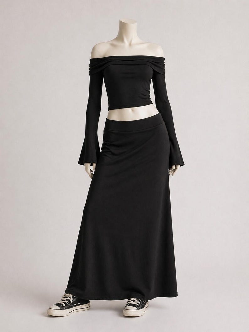 May include: A black off-the-shoulder top with long sleeves and a matching floor-length skirt. The top has a fitted silhouette, and the skirt flows to the ground. The outfit is paired with black and white sneakers.