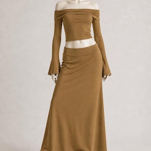 May include: A two-piece outfit in a warm brown hue, consisting of an off-the-shoulder crop top with long, flared sleeves and a matching floor-length skirt. The mannequin is wearing black and white sneakers.