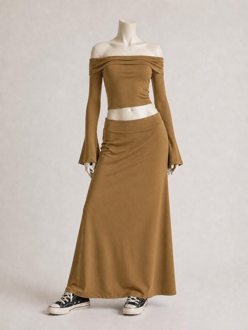 May include: A two-piece outfit in a warm brown hue, consisting of an off-the-shoulder crop top with long, flared sleeves and a matching floor-length skirt. The mannequin is wearing black and white sneakers.
