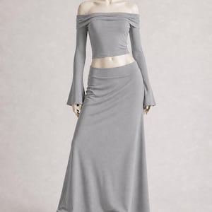 May include: A gray two-piece outfit on a mannequin. The top is an off-the-shoulder crop top with long sleeves. The bottom is a long, flowing skirt. The mannequin is wearing black and white sneakers.