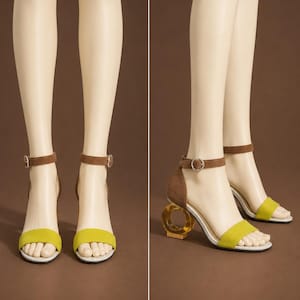 May include: A pair of yellow and brown heeled sandals. The sandals have a yellow strap across the toes and a brown ankle strap with a silver buckle. The heels are a unique gold geometric design.