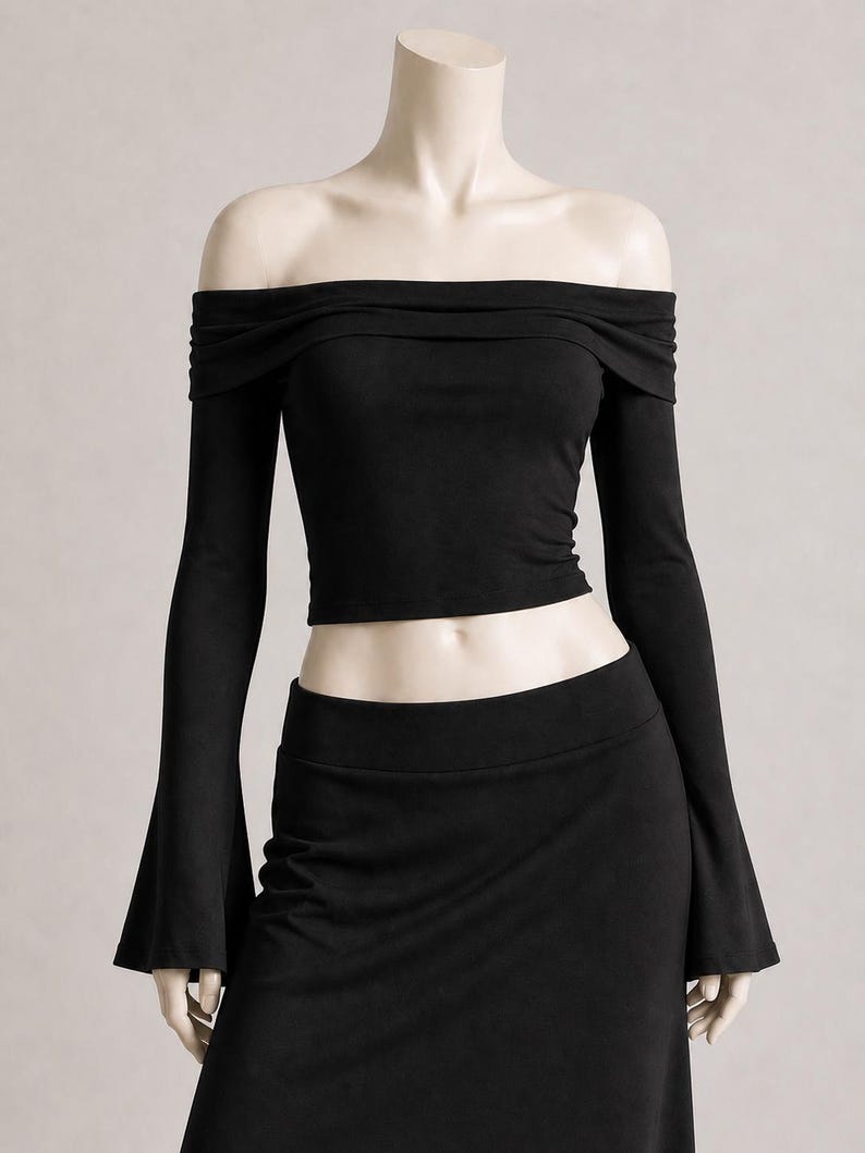 May include: A black off-the-shoulder crop top with long sleeves and a matching black skirt. The top has a gathered neckline and the sleeves flare out at the wrists. The skirt is a simple, fitted design.