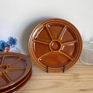 May include: A stack of four brown ceramic serving platters with divided sections. The platters are round with a central circle and six pie-shaped compartments. Each platter has a beaded edge. One platter is on a black metal stand.