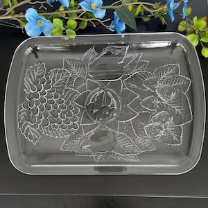 Peut inclure: Un plateau de service rectangulaire en verre transparent orné d'un motif gravé représentant une grappe de raisin, des fraises et des feuilles. Le centre présente un motif circulaire avec des baies, entouré d'une poire et d'une prune.