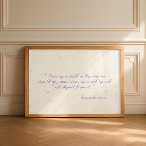 May include: A framed print with a light-colored wooden frame. The print features handwritten blue text on a textured, off-white background. The text is a quote from Proverbs 22:6.