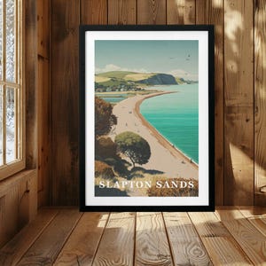 May include: A framed art print featuring a coastal landscape illustration of Slapton Sands. The scene depicts a long sandy beach meeting turquoise water, with rolling green hills in the background, trees in the foreground, and the text SLAPTON SANDS.