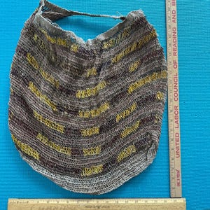 May include: Handmade woven bag in shades of brown and yellow. The bag has a rounded shape with a handle and measures approximately 30 cm wide. The bag is made of a textured material and has a unique, handcrafted appearance.