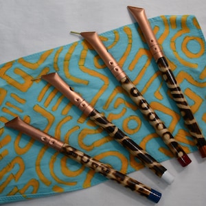 May include: Four decorative pens with copper-colored tips and animal print barrels. The pens rest on a blue and yellow patterned fabric. The pen tips have different colored ends, including red, white, and blue.