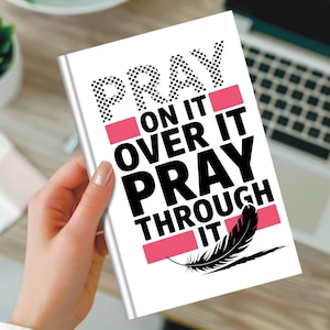 Könnte beinhalten: Ein weißes Notizbuch mit den Worten "PRAY ON IT OVER IT PRAY THROUGH IT" in Schwarz und Rosa. Das Wort "PRAY" hat ein Schachbrettmuster. Eine schwarze Federgrafik befindet sich unten.