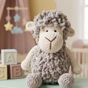 May include: A handmade, plush sheep toy in soft gray and white. The sheep has a fluffy, textured body, a white face, and small ears. It is sitting on a light green surface, with wooden alphabet blocks nearby. A charming nursery decoration.