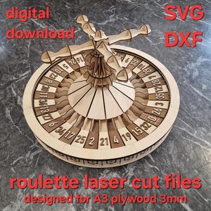 Puede incluir: Una ruleta de madera cortada con láser con números y un mecanismo giratorio central. El diseño incluye el texto "descarga digital", "SVG DXF" y "archivos de corte láser de ruleta diseñados para contrachapado A3 3mm".