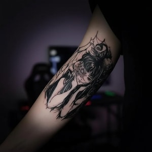 May include: Black and white tattoo of a woman with long hair and a partially obscured face. The tattoo design includes spiderwebs and intricate details, creating a gothic or fantasy theme. The tattoo is on the arm.