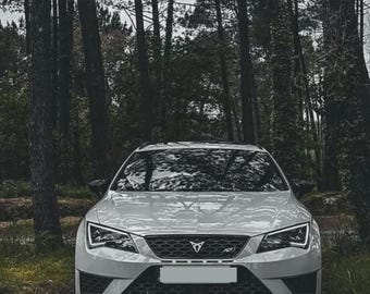 Op de afbeelding: Een witte Cupra SUV gezien vanaf de voorzijde, voorzien van een zwarte honingraatgrille met een centraal koperkleurig logo, scherpe hoekige koplampen met geïntegreerde led-dagrijverlichting en een onderste luchtinlaat met zwart gaas.