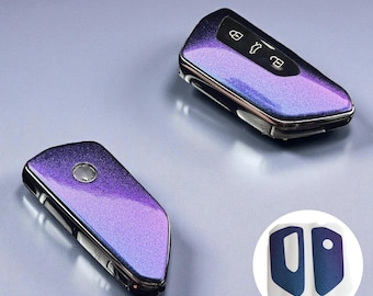 May include: Two car key fobs with a shimmering purple and blue finish. The key fobs have silver trim and feature button icons. A small sticker with two matching key fob covers is in the lower right corner.