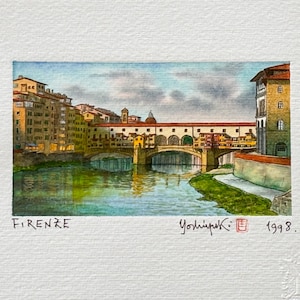 May include: Watercolor painting of the Ponte Vecchio bridge in Florence, Italy. The artwork depicts the bridge over a river, with buildings on either side. The painting is signed and dated 1998.