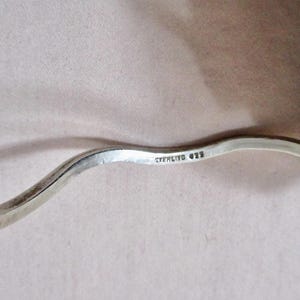 May include: Close-up of a silver, wavy bracelet. The bracelet is stamped with "STERLING 925". The silver has a polished finish. The bracelet is on a neutral background.