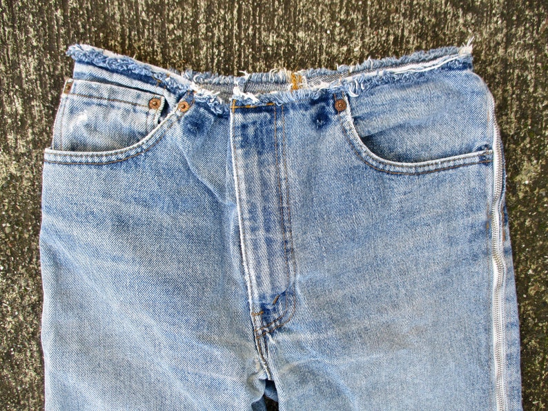 May include: A pair of light blue denim jeans with a frayed hem and a zipper detail on the side seams.