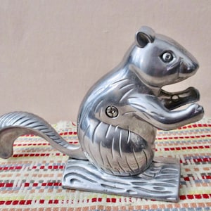 May include: A silver squirrel nutcracker with a detailed design. The squirrel is sitting on a base and has a long tail that acts as a lever to crack nuts.