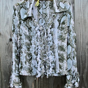 May include: A long-sleeved blouse with a snake print pattern. The blouse has a ruffled neckline and cuffs. The blouse is white and green.