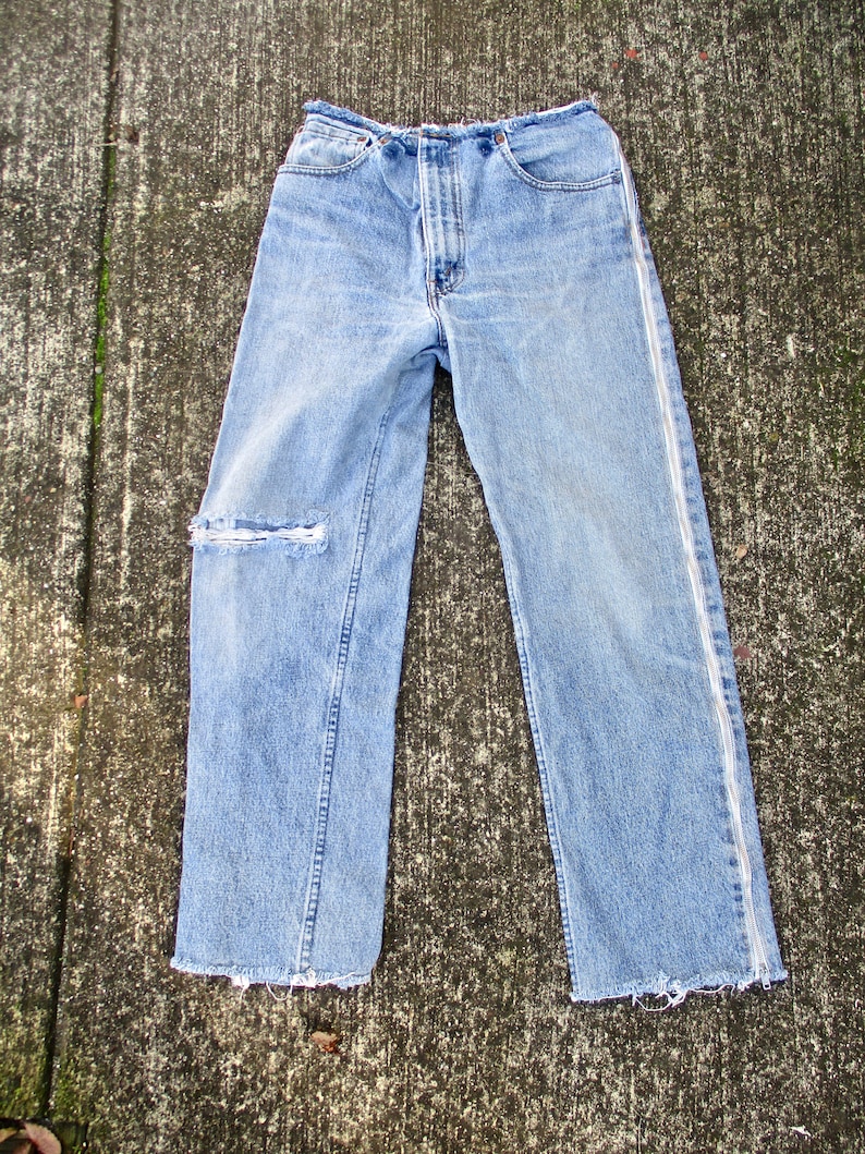 May include: A pair of light blue denim jeans with a white seam down the outside of each leg. The jeans have a distressed look with a small rip on one leg and frayed hems.