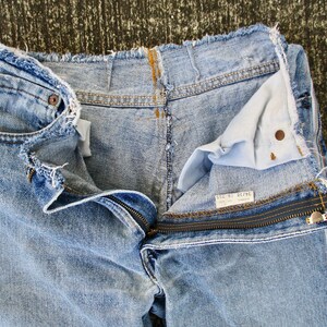 May include: Light blue denim jeans with a zipper detail and frayed edges. The jeans are turned inside out, revealing the lining and a label that reads "Size 31 Regular".