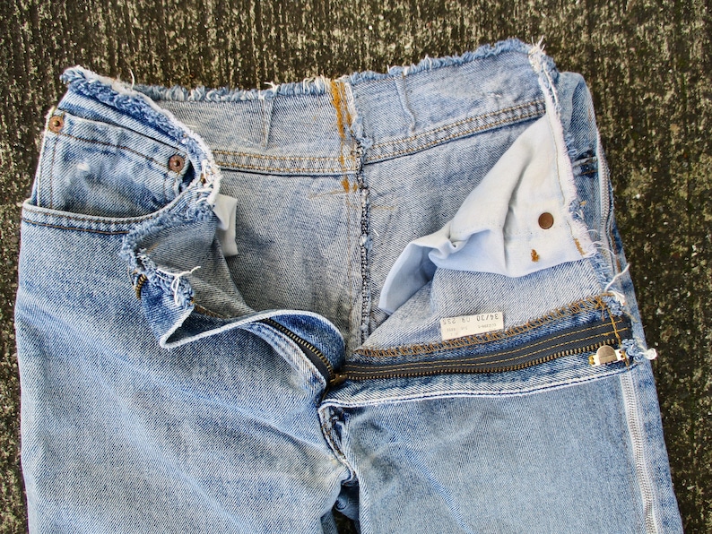 May include: Light blue denim jeans with a zipper detail and frayed edges. The jeans are turned inside out, revealing the lining and a label that reads "Size 31 Regular".