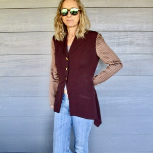 May include: A woman wearing a maroon blazer with brown and white striped sleeves, blue jeans, and sunglasses.