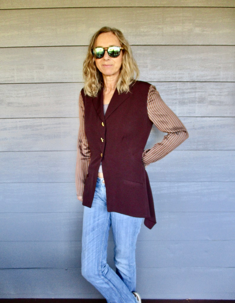 May include: A woman wearing a maroon blazer with brown and white striped sleeves, blue jeans, and sunglasses.