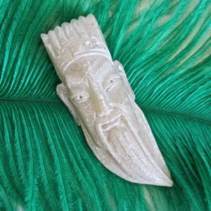 May include: A white stone sculpture of a man's face with a beard, against a green feather background.