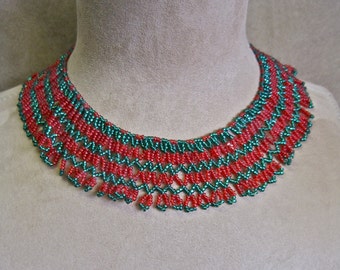 May include: A red and green beaded necklace with a scalloped edge. The necklace is made of small, round beads and is arranged in a pattern of alternating red and green beads.