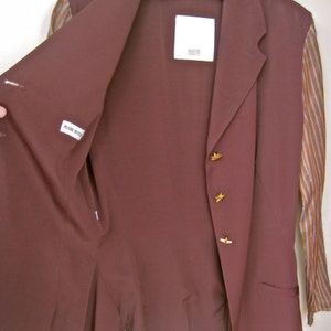 May include: A maroon blazer with gold buttons and a striped lining. The blazer has a label that says "Made in Italy" and another label that says "Roberto Cavalli".