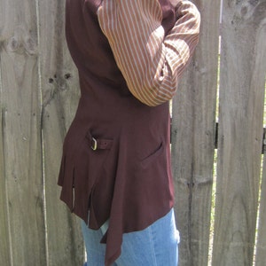 May include: A maroon waistcoat with a brown and white striped sleeve. The waistcoat has a long, flowing back and a belt buckle on the side.