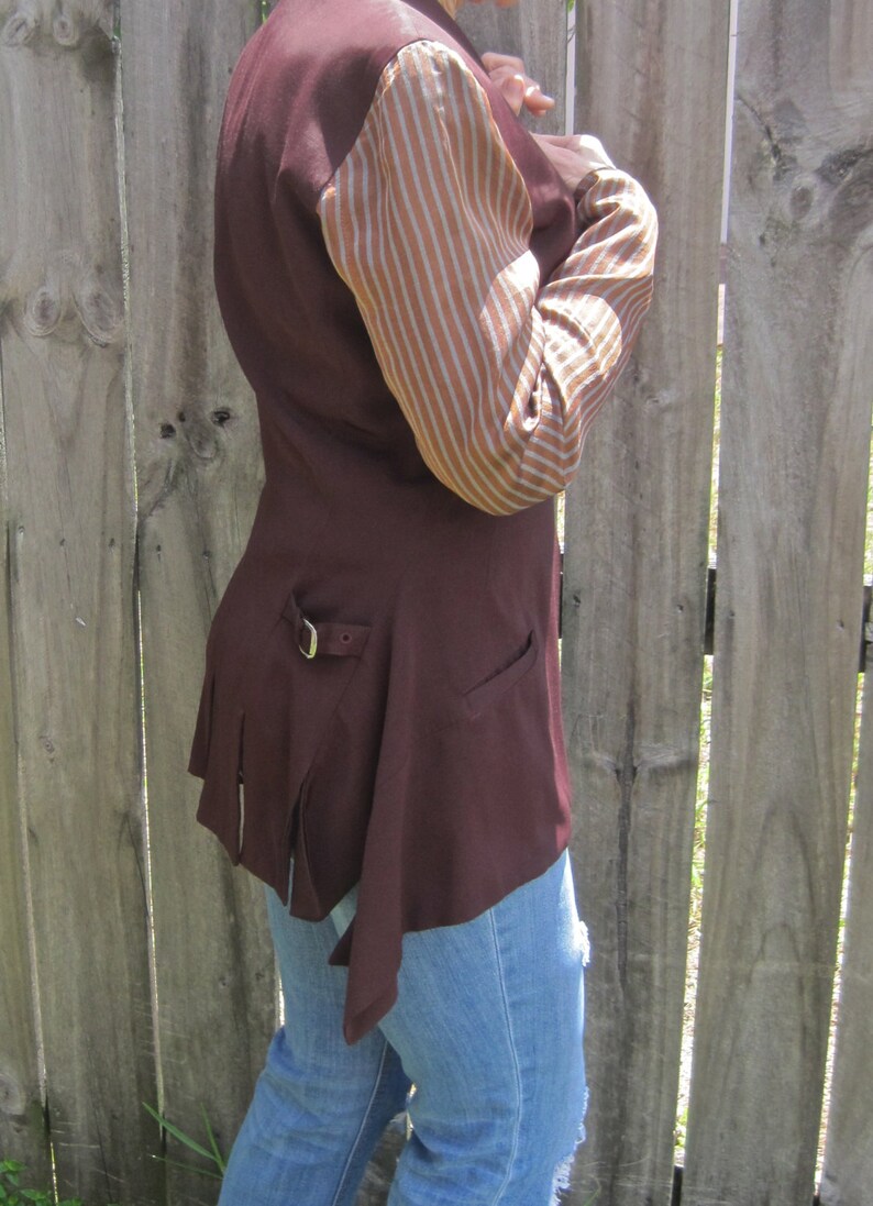 May include: A maroon waistcoat with a brown and white striped sleeve. The waistcoat has a long, flowing back and a belt buckle on the side.