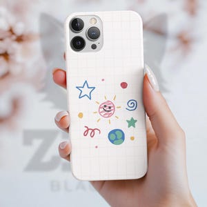 May include: A white phone case with a grid pattern and colorful doodles of a star, sun, planet, and swirls. The case is held in a hand, showcasing the design.