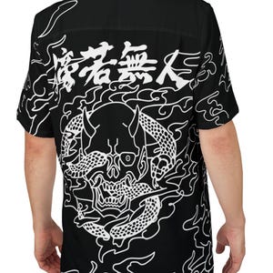 Op de afbeelding: Zwart overhemd met een witte afbeelding op de rug. De afbeelding toont een schedel met hoorns en slangen, omringd door vlammen en Japanse tekst. Het overhemd heeft korte mouwen.