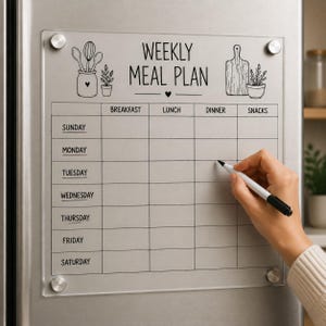 May include: A clear acrylic weekly meal plan board with black printed text and illustrations of kitchen utensils and plants. The grid features columns for breakfast, lunch, dinner, and snacks, and rows for each day of the week, secured by four silver mounts.