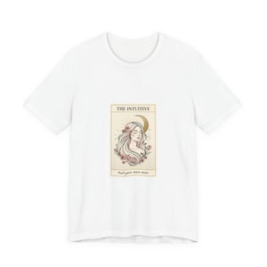 May include: White t-shirt featuring a tarot card design. The card depicts a woman with long hair, a crescent moon, and floral accents. The text on the card reads "THE INTUITIVE" and "trust your inner moon."