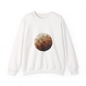 May include: Cream-coloured crew neck sweatshirt with a circular graphic. The graphic features a gradient of brown and beige hues, resembling a textured landscape. The sweatshirt has long sleeves and a relaxed fit, suitable for casual wear.