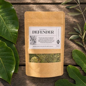 May include: A brown paper pouch containing a botanical tea blend labeled DEFENDER by Present Body Co. The label lists ingredients including soursop, avocado, guava, olive, mulberry, and fig leaves, with a net weight of 1 oz printed on the front.