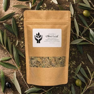 Puede incluir: Una bolsa de papel marrón que contiene hojas de olivo secas con una ventana transparente. La etiqueta blanca presenta el texto Present Body Co. Olive Leaf, Dried Cut Fruit Leaf, Single Botanical Tea Ingredient, Net Wt 1 oz (28g).