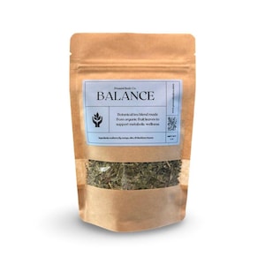 May include: A brown paper pouch of botanical tea labeled "BALANCE." The light blue label includes the text "Present Body Co." and "Botanical tea blend made from organic fruit leaves to support metabolic wellness." The pouch contains dried green tea leaves.
