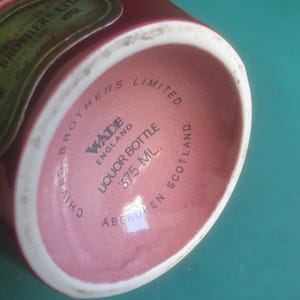 May include: A maroon liquor bottle with a white rim. The base of the bottle features the text "CHIVAS BROTHERS LIMITED" and "WADE ENGLAND LIQUOR BOTTLE 375 ML. ABERDEEN SCOTLAND."