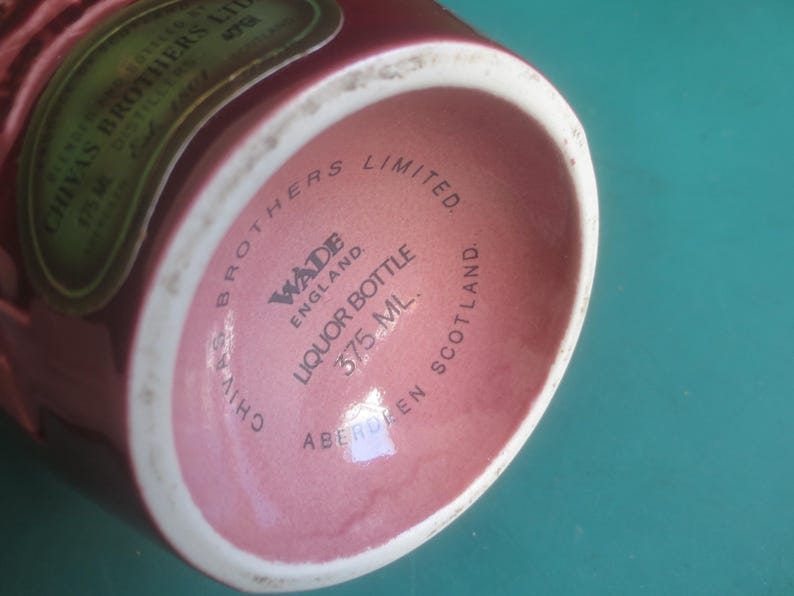 May include: A maroon liquor bottle with a white rim. The base of the bottle features the text "CHIVAS BROTHERS LIMITED" and "WADE ENGLAND LIQUOR BOTTLE 375 ML. ABERDEEN SCOTLAND."
