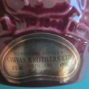 May include: Close-up of a maroon-colored bottle with a gold label. The label reads "CHIVAS BROTHERS LTD" and "375 ML". The bottle is from Scotland, established in 1801.