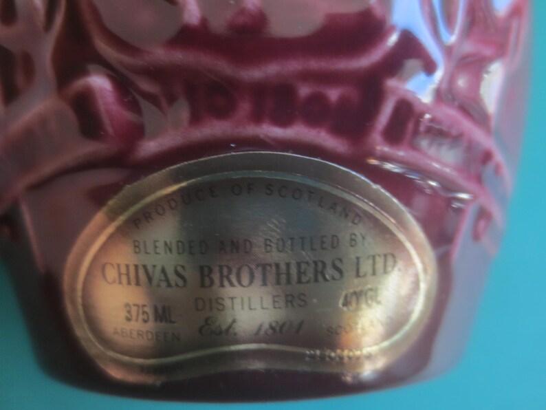 May include: Close-up of a maroon-colored bottle with a gold label. The label reads "CHIVAS BROTHERS LTD" and "375 ML". The bottle is from Scotland, established in 1801.