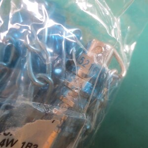 Puede incluir: Primer plano de una bolsa de pl&aacute;stico transparente que contiene m&uacute;ltiples componentes met&aacute;licos peque&ntilde;os de color azul. Los componentes parecen estar conectados por peque&ntilde;os bucles met&aacute;licos. Uno de los componentes tiene el n&uacute;mero "52" impreso.