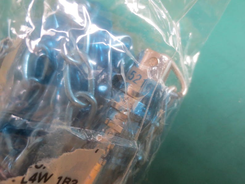 Puede incluir: Primer plano de una bolsa de pl&aacute;stico transparente que contiene m&uacute;ltiples componentes met&aacute;licos peque&ntilde;os de color azul. Los componentes parecen estar conectados por peque&ntilde;os bucles met&aacute;licos. Uno de los componentes tiene el n&uacute;mero "52" impreso.