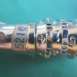 Puede incluir: Primer plano de un candado de combinaci&oacute;n plateado con un lazo de metal. Los n&uacute;meros 5216 son visibles en una etiqueta blanca y azul. Los diales de combinaci&oacute;n est&aacute;n grabados con n&uacute;meros.